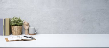 Kitapları, kahve fincanı, gözlükleri ve beyaz masasında saksı bitkisi olan şık bir iş yeri. Reklam metniniz için alanı kopyalayın.