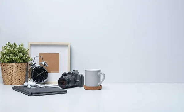 Home office desk with empty picture frame, camera, coffee cup and potted plant on white table. Copy space for your advertise text.