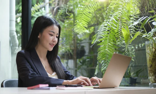 若いアジアの女性のオフィス労働者は明るいオフィスに座って コンピュータのラップトップで働いています — ストック写真