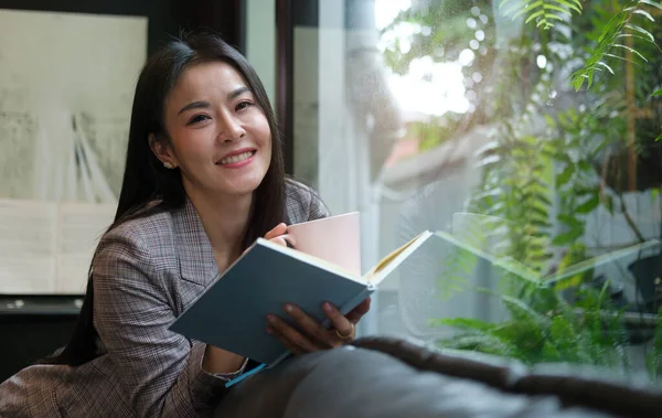 Happy Young Woman Relaxing Sofa Front Window Reading Book Drinking — Stock Photo, Image