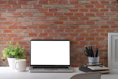 Laptop bilgisayar, kahve fincanı, resim çerçevesi ve saksı bitkisi beyaz masada. Reklam metniniz için boş ekran.