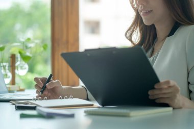 Kırpılmış Asyalı iş kadını ofis masasında oturuyor ve iş belgelerini kontrol ediyor..