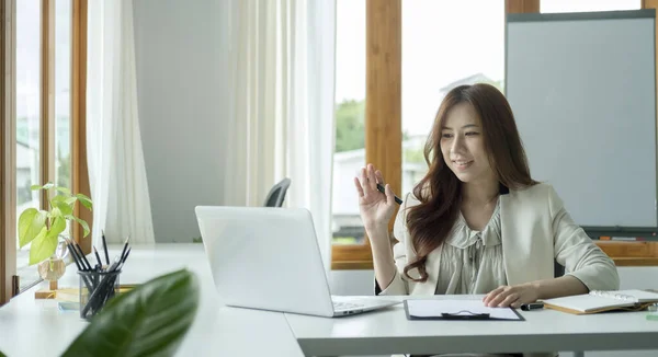 Smiling business woman waving hand and having video call via laptop in the office.