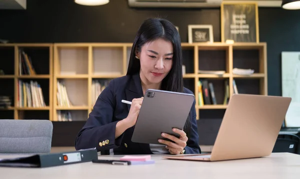 Successful businesswoman sitting front of laptop computer and using digital tablet.