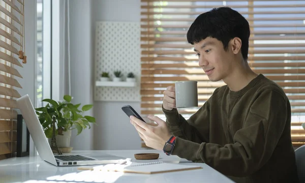 Relaxed Asian Man Drinking Coffee Checking Social Media Smart Phone — 图库照片