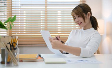 Attractive woman sitting front of laptop, taking notes working on financial report at her workplace.	