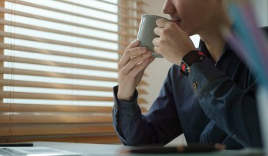 Huzurlu genç işadamı kahve içiyor ve ofis penceresinden dışarı bakıyor..