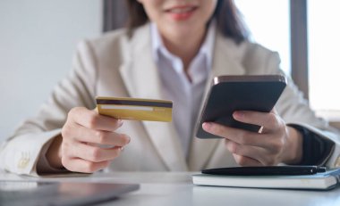 İnternet bankacılığı veya internet üzerinden alışveriş yapmak için elinde kredi kartı ve akıllı telefon tutan gülümseyen genç kadın.