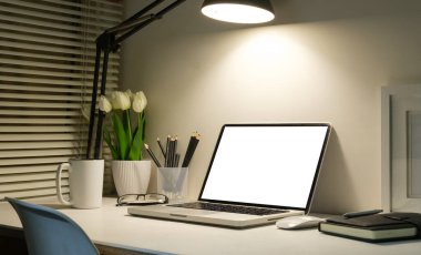 Ev bilgisayarı, resim çerçevesi, ev bitkisi ve kahve fincanı beyaz masada..