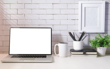 Boş ekranlı dizüstü bilgisayar, kahve fincanı, defter ve ev bitkisi parlak, modern iş yerinde beyaz masada..