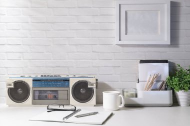 Klasik radyo, kahve fincanı, defter ve saksı bitkisi pencereden gün ışığı alan beyaz masanın üzerinde. Reklam metni için alanı kopyala.