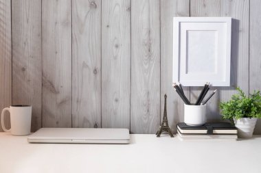 Dizüstü bilgisayar, kahve fincanı, ev bitkisi ve kırtasiye malzemesi beyaz masada..