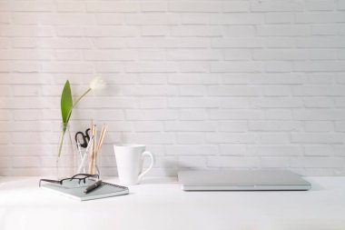 Laptop, kahve fincanı ve beyaz masadaki kırtasiyeli en az iş yeri..