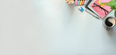 Düz defterler, bir fincan kahve, bardaklar ve kalemler beyaz ofis masasının üzerinde duruyordu. Kopyalama alanı olan üst görünüm.
