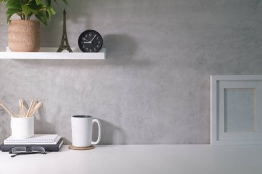Home office desk with picture frame, coffee cup, glasses and supplies on white table.