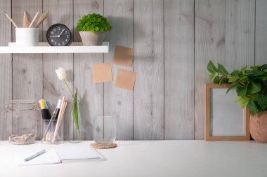 Home office desk with potted plants, stationery and picture frame.