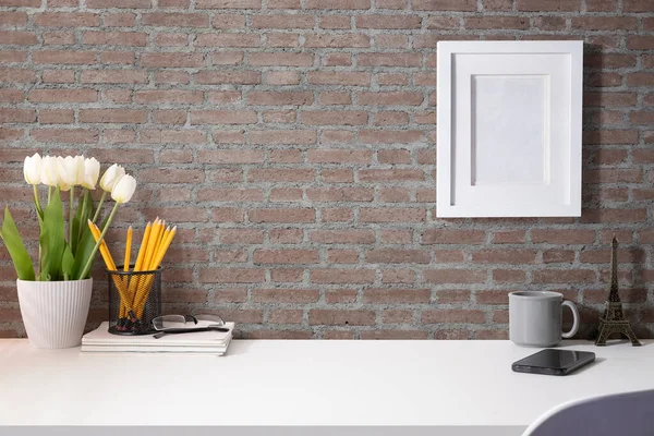 Resim çerçeveli, kahve fincanı, ev bitkisi ve beyaz masadaki kırtasiyeli şık bir iş yeri..