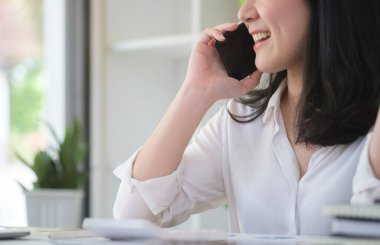 Satisfied businesswoman sitting at her workplace and talking on mobile phone.