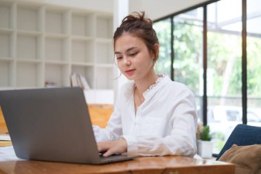 Milenyum Asyalı iş kadını dizüstü bilgisayar kullanıyor ve ofiste mali belgeler üzerinde çalışıyor..