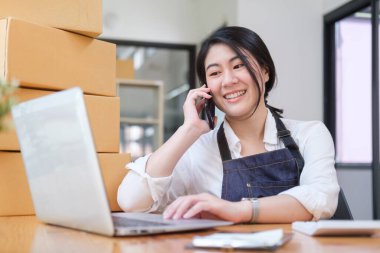 Başlangıçta küçük işletme girişimcisi cep telefonuyla konuşuyor ve çevrimiçi alımları bilgisayarda kontrol ediyor.