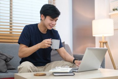 Asian man freelancer in casual clothes browsing internet, replies to email or working online via laptop computer.