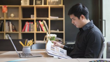 Focused asian male interior designer working with colour swatches and laptop computer at creative office.
