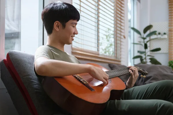 Jeune Homme Asiatique Jouer Guitare Tout Étant Assis Sur Canapé — Photo