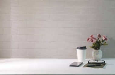 Comfortable workplace with paper cup, flower pot, smart phone and notebook on white table. Copy space for your advertise text.