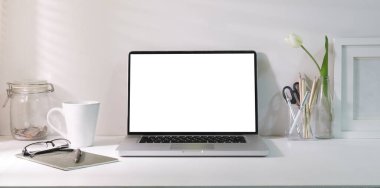 Laptop computer with empty screen, coffee cup, picture frame and stationery on white table.