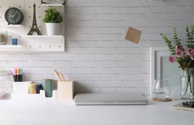 Creative workplace with laptop, picture frame, flower pot and stationery on white table.