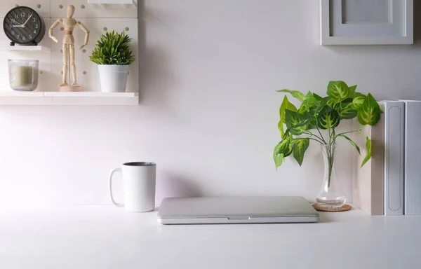 Creative workplace with laptop, picture frame, flower pot and stationery on white table.