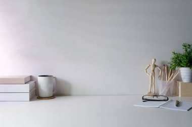 Comfortable workplace with books, cup of coffee, glasses and houseplant on white table.