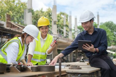 Engineers and Architect in protective hardhats working and discussing detail of design project  together.