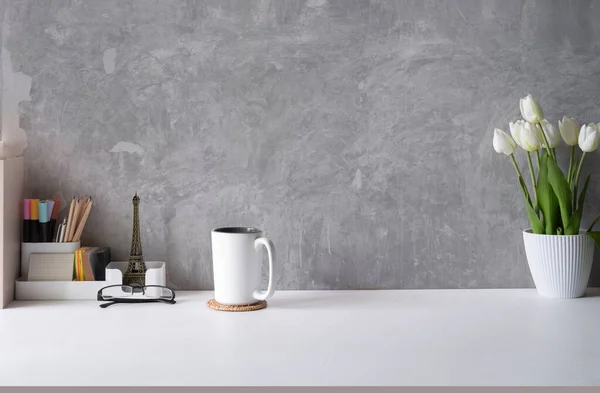 Stylish workplace, home office desk with cup of coffee, flower pot and supplies on white table. Copy space for your text.