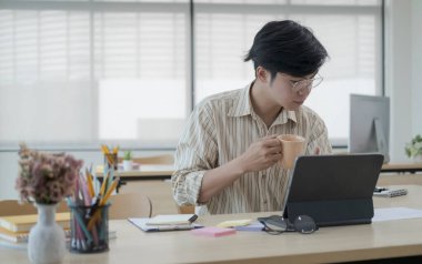 Focused asian male interior designer working with colour swatches and laptop computer at creative office.