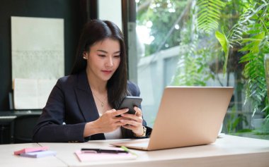 Charming businesswoman sitting in comfortable workplace and using smart phone.	