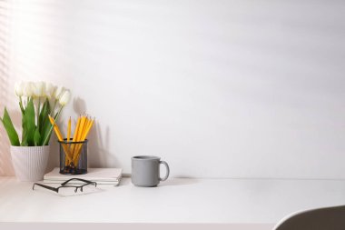 Feminine modern workplace with flower pot, coffee cup and pencil holder on white table. Copy space for your advertise text.