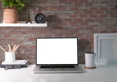 Mockup laptop with blank screen, coffee cup, houseplant and supplies on white table.