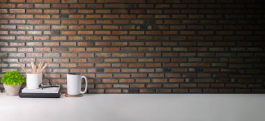 Stylish, creative workplace with books, coffee cup and potted plant on white table against brick wall.  Copy space for your advertise text. 