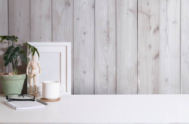Blank picture frame, coffee cup, houseplant and supplies on white table. Copy space for your advertise text.