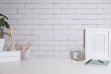 Blank picture frame, glass of water, books and houseplant on white table.