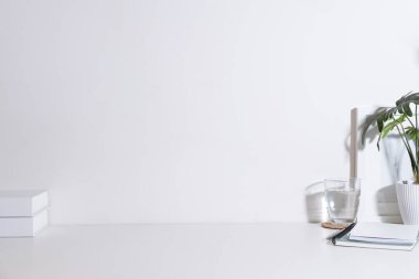 Minimal workplace with books, glass of water and potted plant on white table. Copy space for your text.