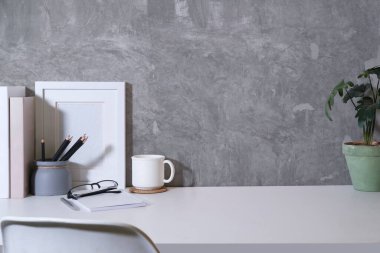 Stylish workplace with books, coffee cup, picture frame and potted plant on white table. Copy space for your text.