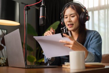 Young female podcaster broadcasting live audio podcast in her home studio at night.