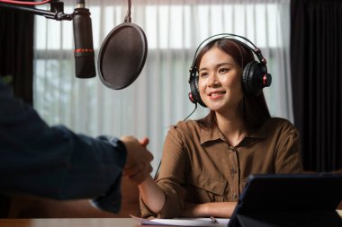 Friendly woman radio host shaking hands with guest after interviewing in live streaming podcast.