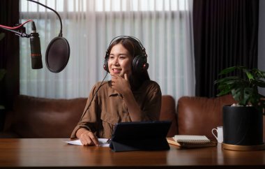Beautiful young woman radio host listening to interesting conversation from guest while streaming audio podcast.