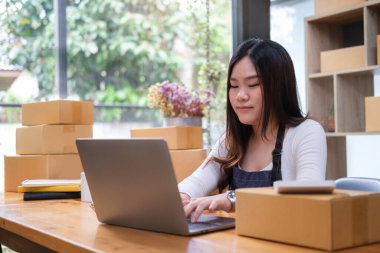 Young online seller confirming orders from customer on laptop computer. Online selling and e-commerce business concept.