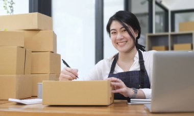 Gülümseyen genç bir kadın küçük bir işletme sahibi olarak karton kutuya adres yazmaya başladı..