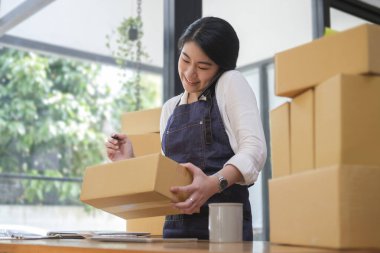 Young female online seller confirming orders from customer on mobile phone.	