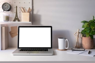 Front view laptop with blank screen, houseplant, coffee cup  and office supplies on white table.